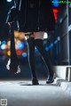 A woman in a black coat and black stockings walking down a street.