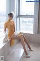 A woman in a yellow dress sitting on a window sill.