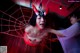 A woman in a devil costume is hanging from a spider web.