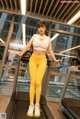 A woman in a white top and yellow leggings standing on a treadmill.