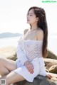 A woman sitting on a rock by the water.