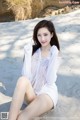 A woman in a white dress sitting on a beach.