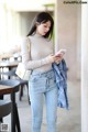 a woman in jeans and a turtleneck is looking at her phone