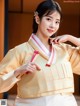 A woman in a yellow and white hanbok poses for a picture.