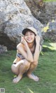 A woman in a bikini and hat sitting on the grass.