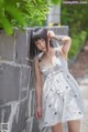 A woman in a white dress leaning against a wall.