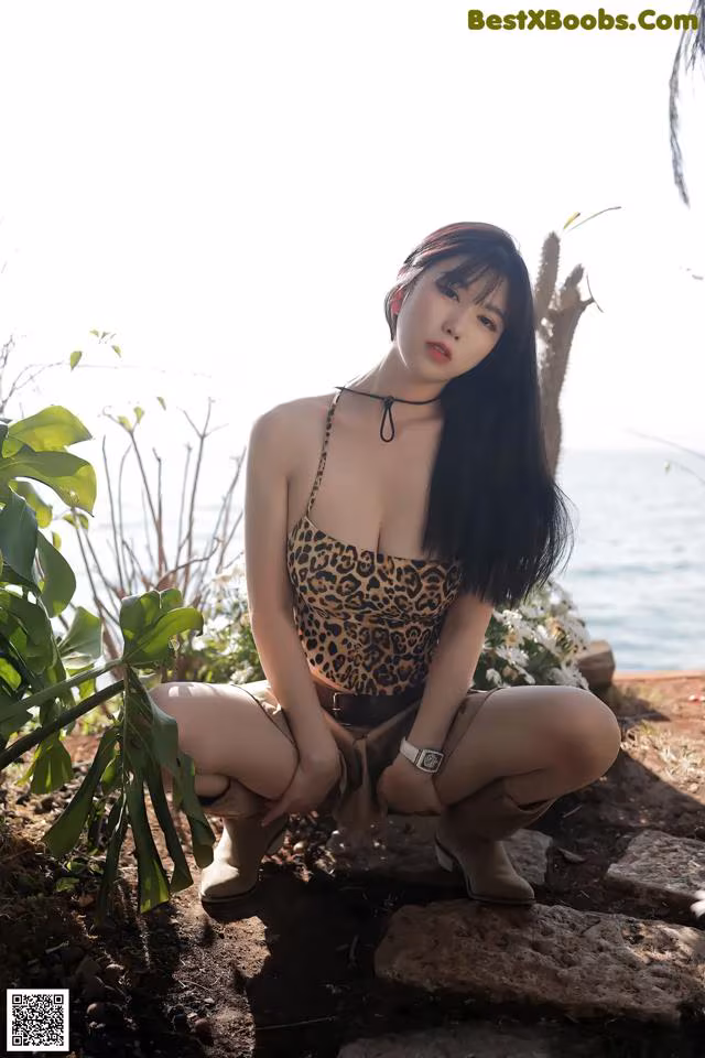 A woman in a leopard print bathing suit sitting on a rock.