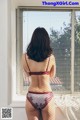 A woman in a red bra and panties standing by a window.