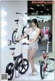 A woman standing next to a bike on display.