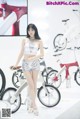 A woman standing next to a bike on display.