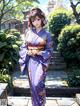 A woman in a purple kimono standing in a garden.