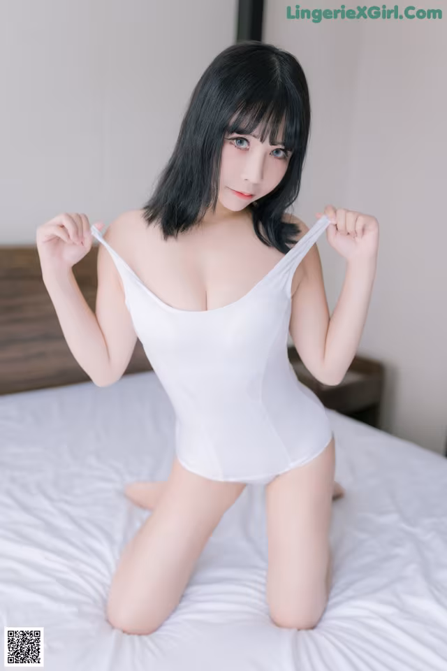 A woman in a white bodysuit sitting on a bed.