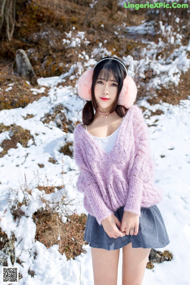 A woman wearing a pink sweater and ear muffs standing in the snow.