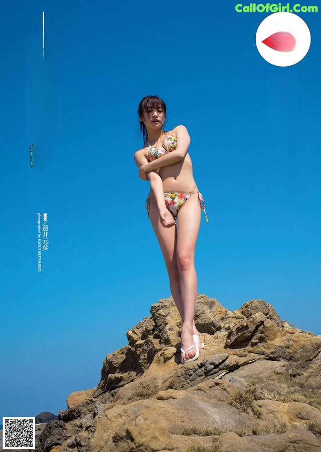 A woman in a bikini standing on a rock by the ocean.