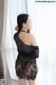 A woman in a black lingerie standing by a window.