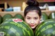 A young girl holding two large watermelons in front of her face.