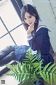 A woman in a school uniform sitting next to a plant.