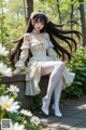 A woman in a white dress sitting on a wall in a park.