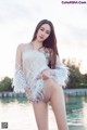 A woman in a white dress posing by the water.